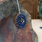 Zuni lapis cluster pendant and pin by Lorraine Waatsa featuring deep blue lapis stones arranged in concentric circles with twisted and sculptural silver detailing; side view.
