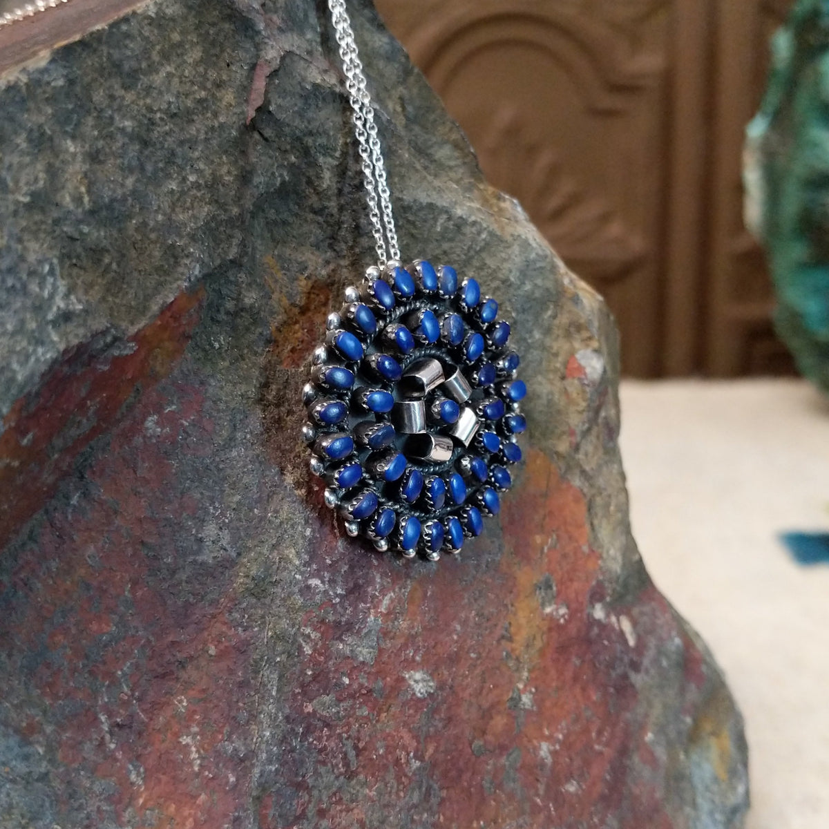 Zuni lapis cluster pendant and pin by Lorraine Waatsa featuring deep blue lapis stones arranged in concentric circles with twisted and sculptural silver detailing; side view.