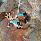 Large Zuni roadrunner pendant and pin by K.E. featuring turquoise, red-orange, black, cream, and patterned shell inlay with sculpted silver legs, beak, wings, and tail; side view.