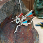 Large Zuni roadrunner pendant and pin by K.E. featuring turquoise, red-orange, black, cream, and patterned shell inlay with sculpted silver legs, beak, wings, and tail; side view.