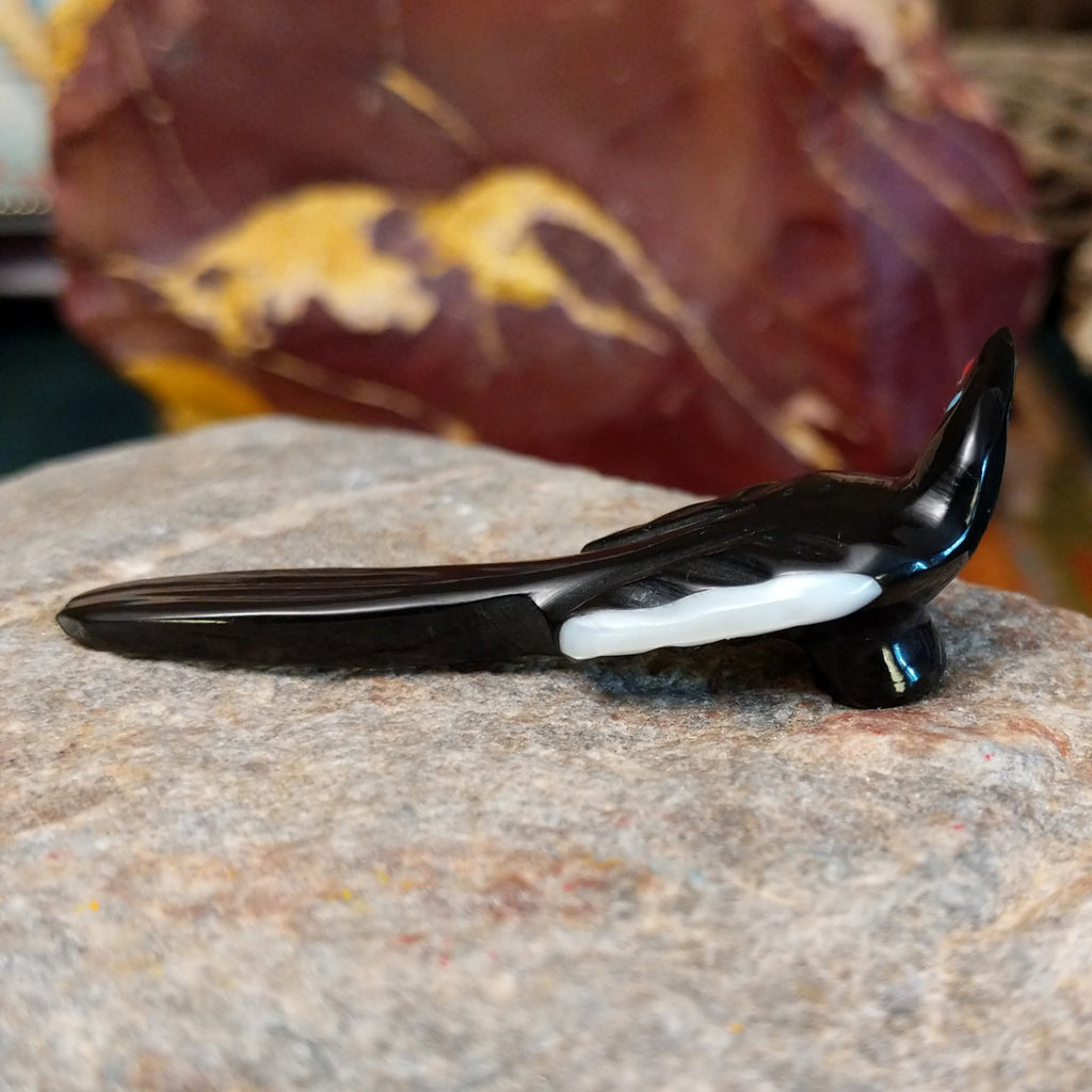 Black marble with mother of pearl inlays carved into a magpie eating a painted, red fruit.