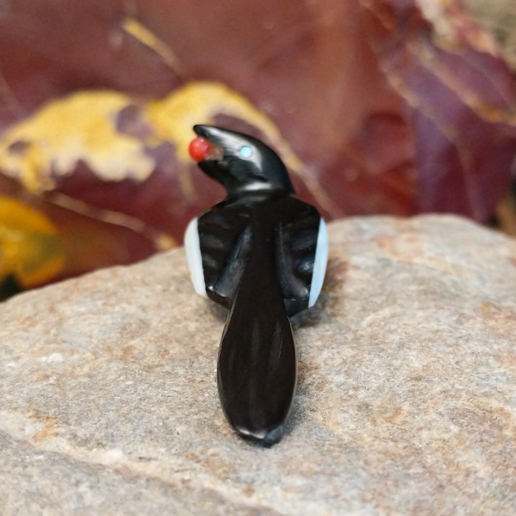 Black marble with mother of pearl inlays carved into a magpie eating a painted, red fruit.