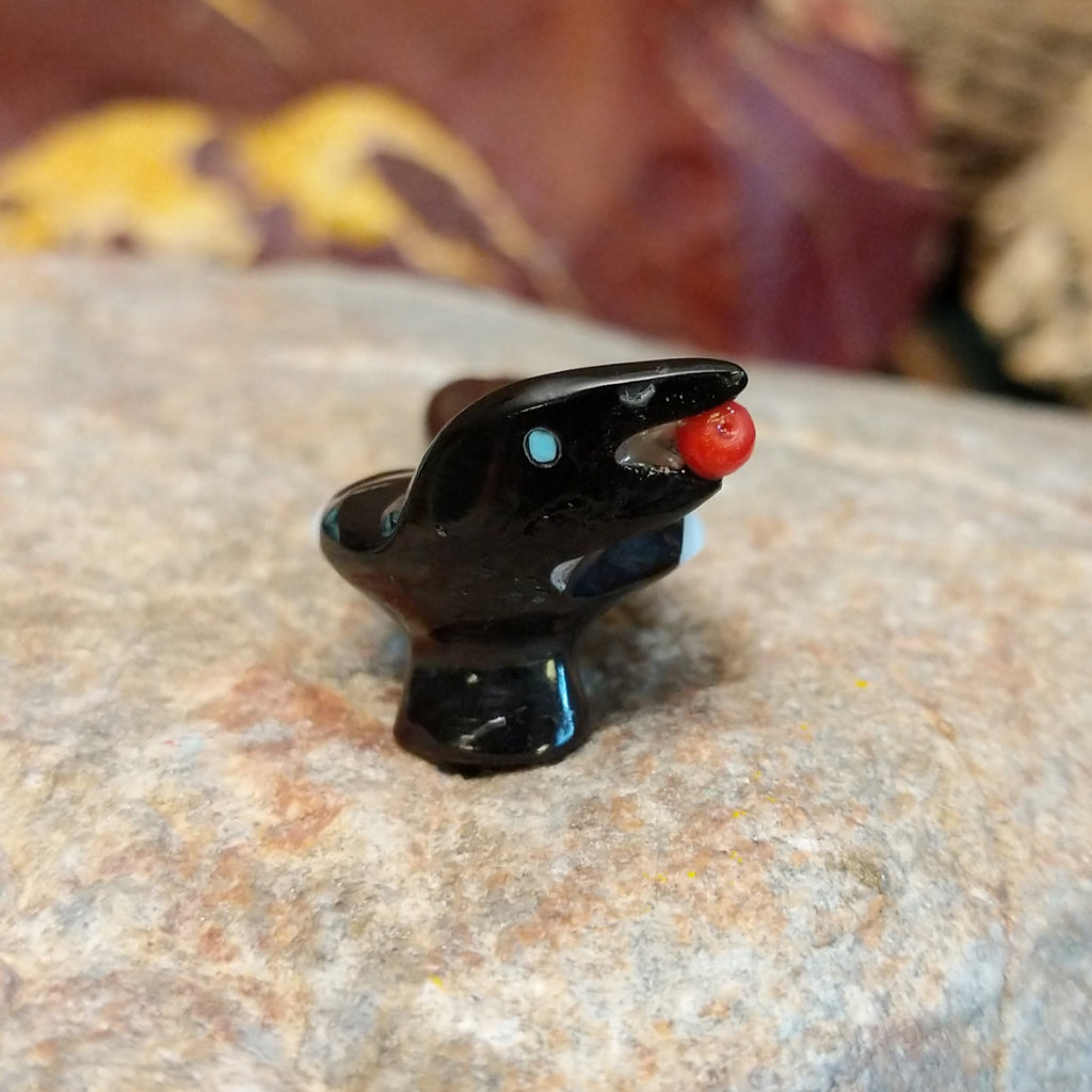 Black marble with mother of pearl inlays carved into a magpie eating a painted, red fruit.