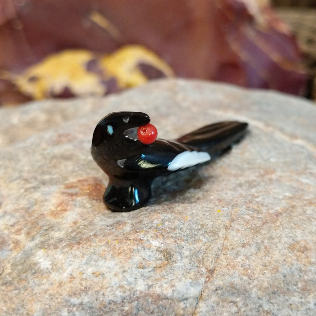 Black marble with mother of pearl inlays carved into a magpie eating a painted, red fruit.