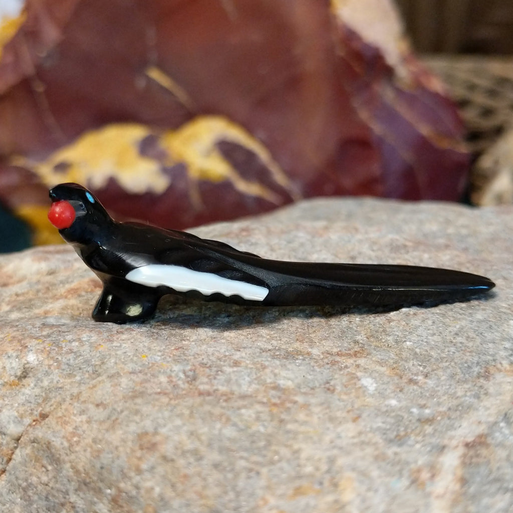 Black marble with mother of pearl inlays carved into a magpie eating a painted, red fruit.