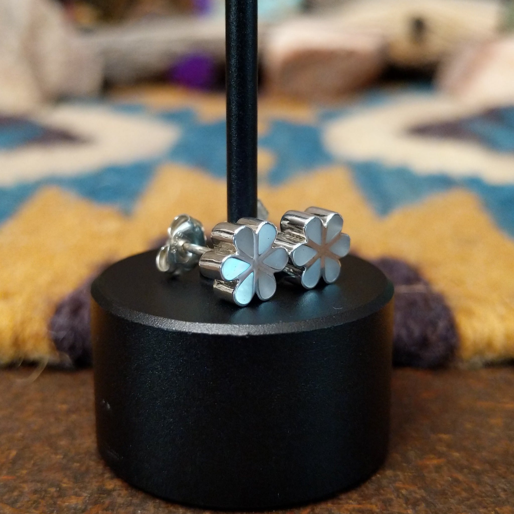 Handcrafted Zuni sterling silver flower earrings by Aaron Lasiloo featuring iridescent mother of pearl inlay in a delicate floral design with polished silver detailing; side view.