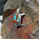 Zuni multistone turtle pendant and pin by W.J.H. featuring colorful turquoise, red-orange, black, and cream inlay set in a detailed silver turtle design; side view.