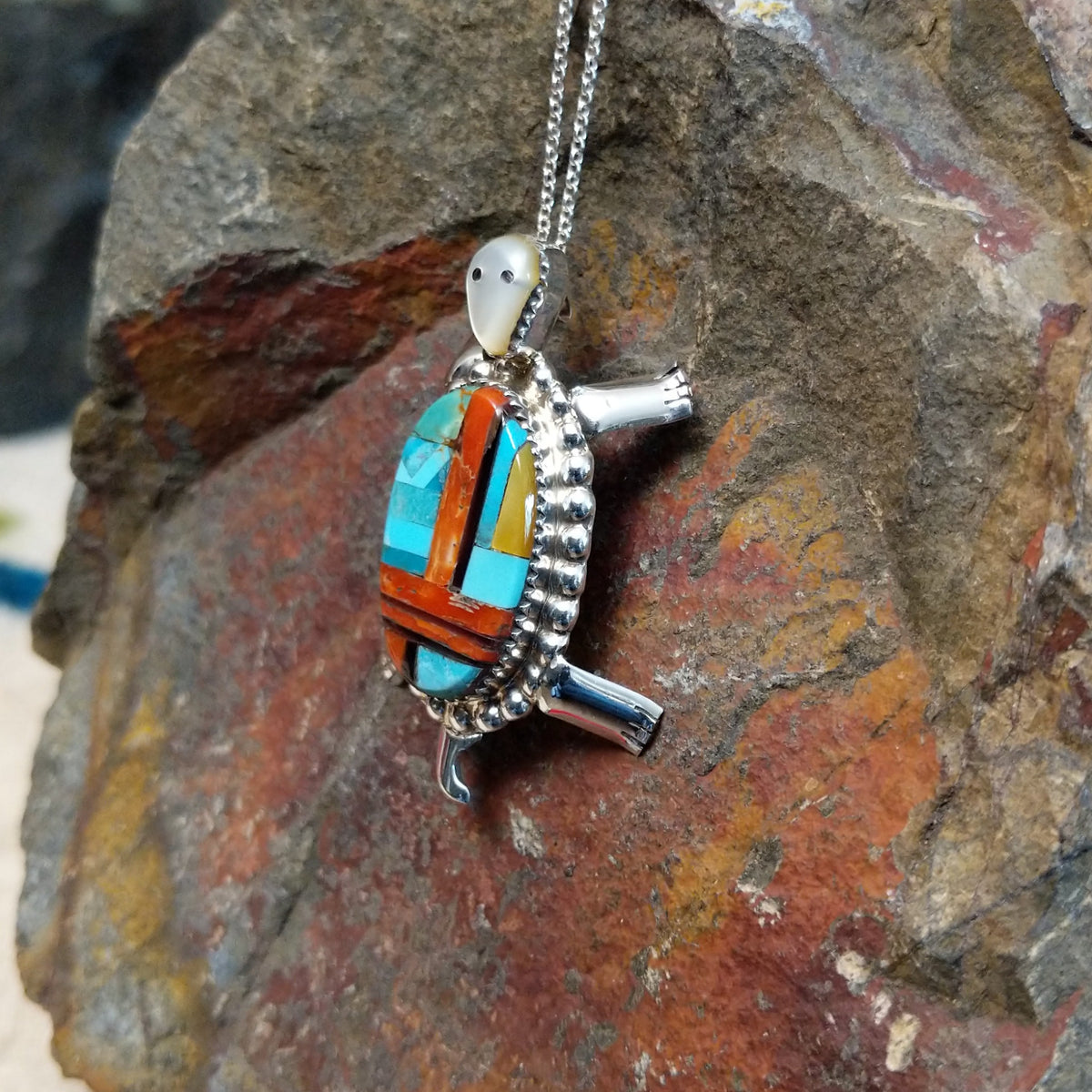 Zuni multistone turtle pendant and pin by W.J.H. featuring colorful turquoise, red-orange, black, and cream inlay set in a detailed silver turtle design; side view.