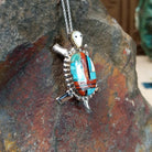 Zuni multistone turtle pendant and pin by W.J.H. featuring colorful turquoise, red-orange, black, and cream inlay set in a detailed silver turtle design; side view.