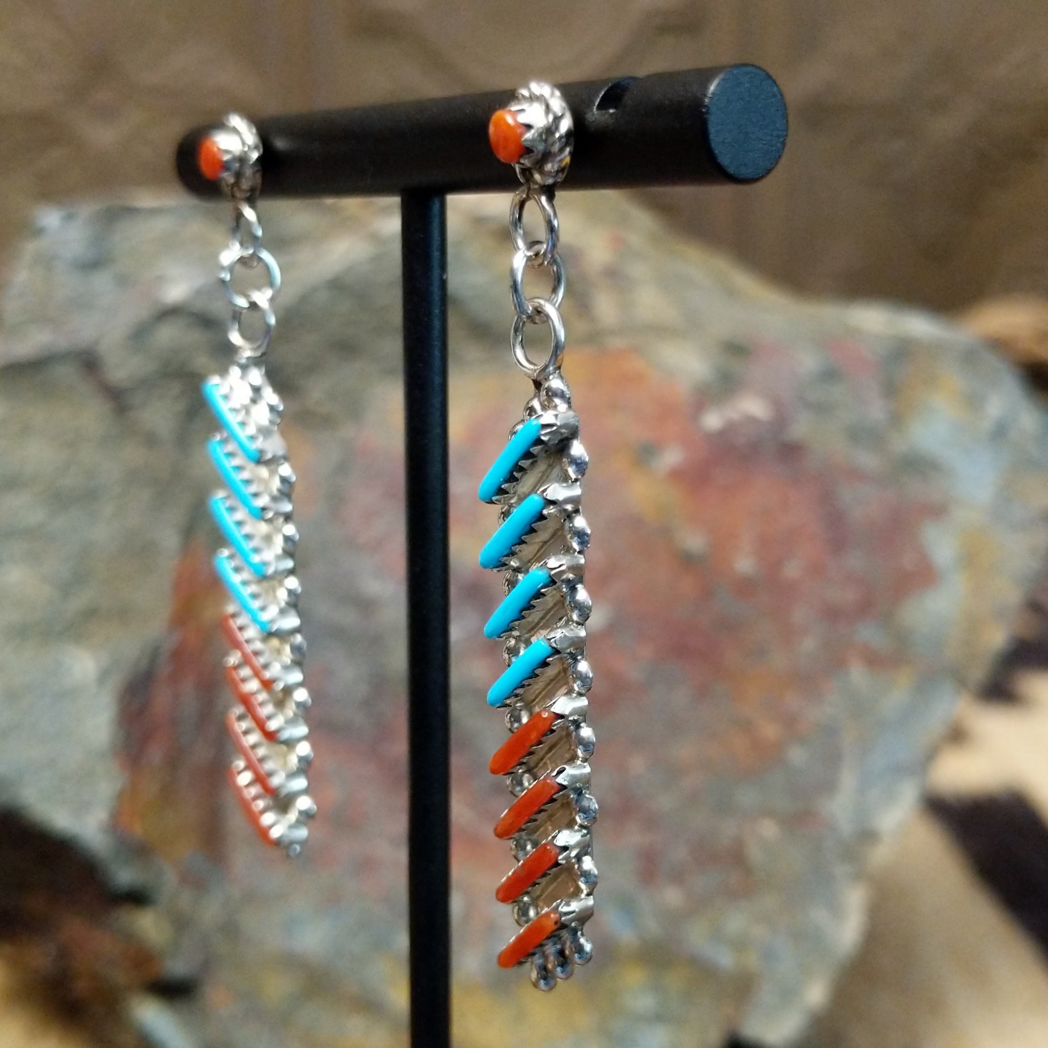 Handcrafted sterling silver Zuni turquoise and coral needlepoint earrings by Lamar Peywa, featuring elongated dangle inlay with coral stud tops; side view.