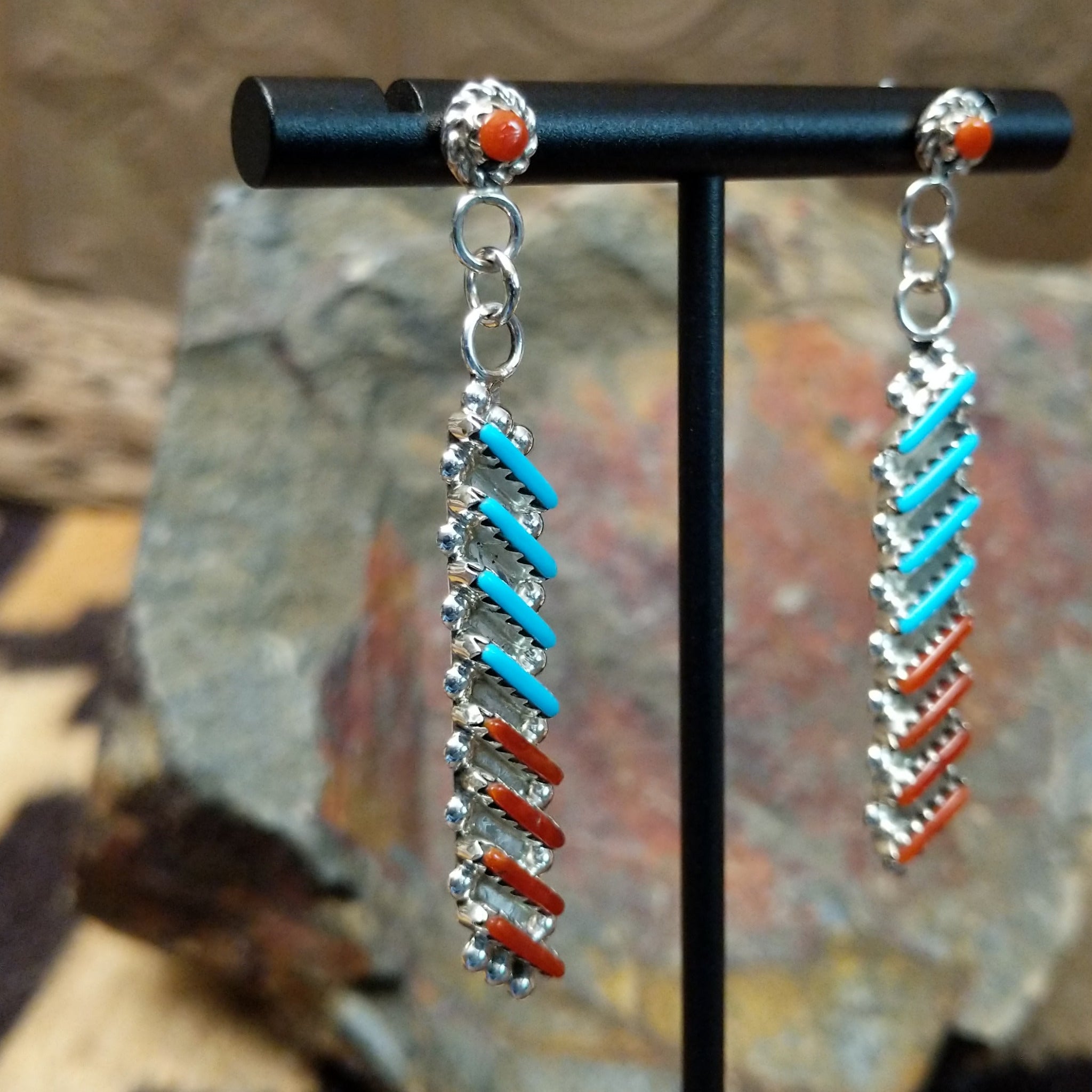 Handcrafted sterling silver Zuni turquoise and coral needlepoint earrings by Lamar Peywa, featuring elongated dangle inlay with coral stud tops; side view.