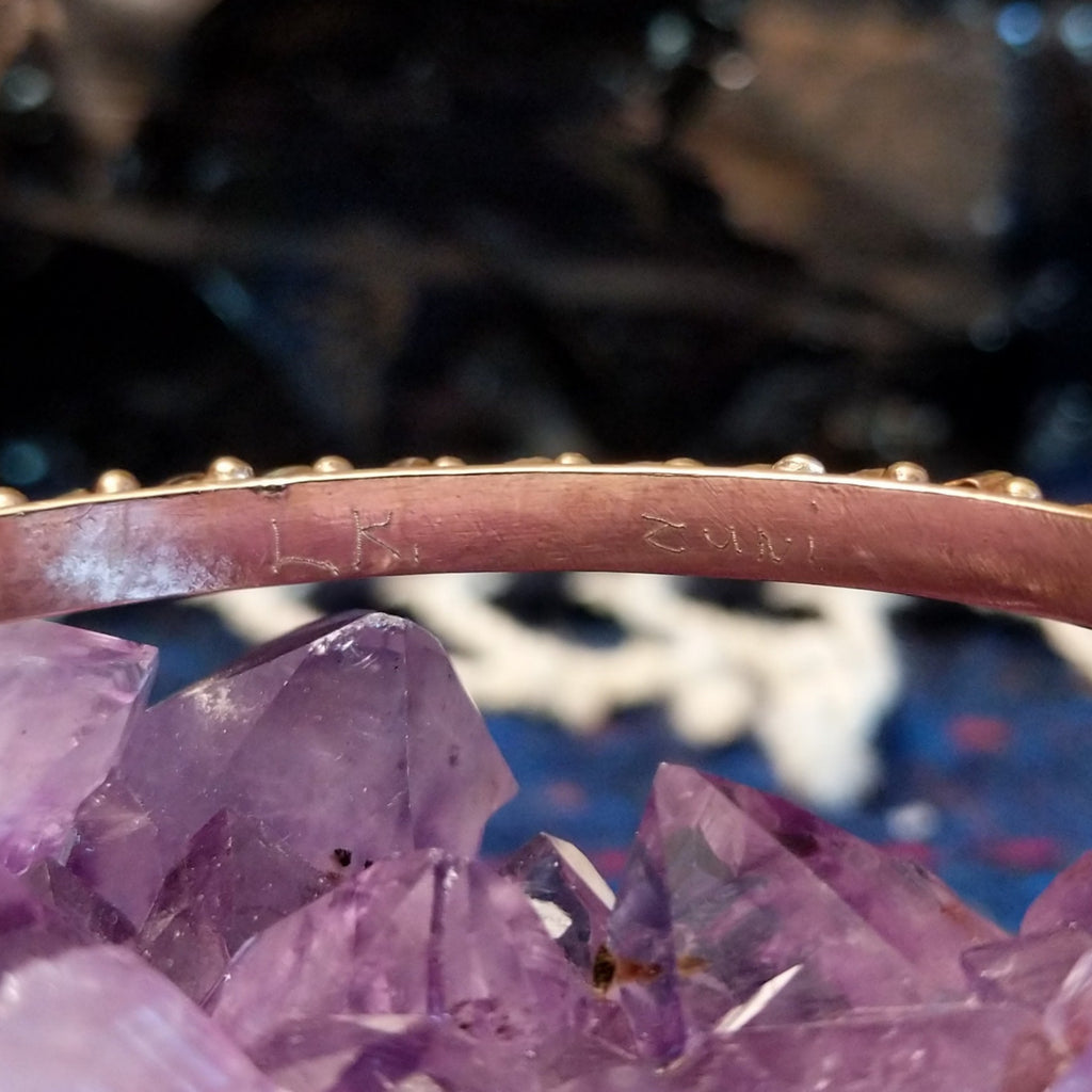 The artist's signature is found on the inner side of the gold cuff.