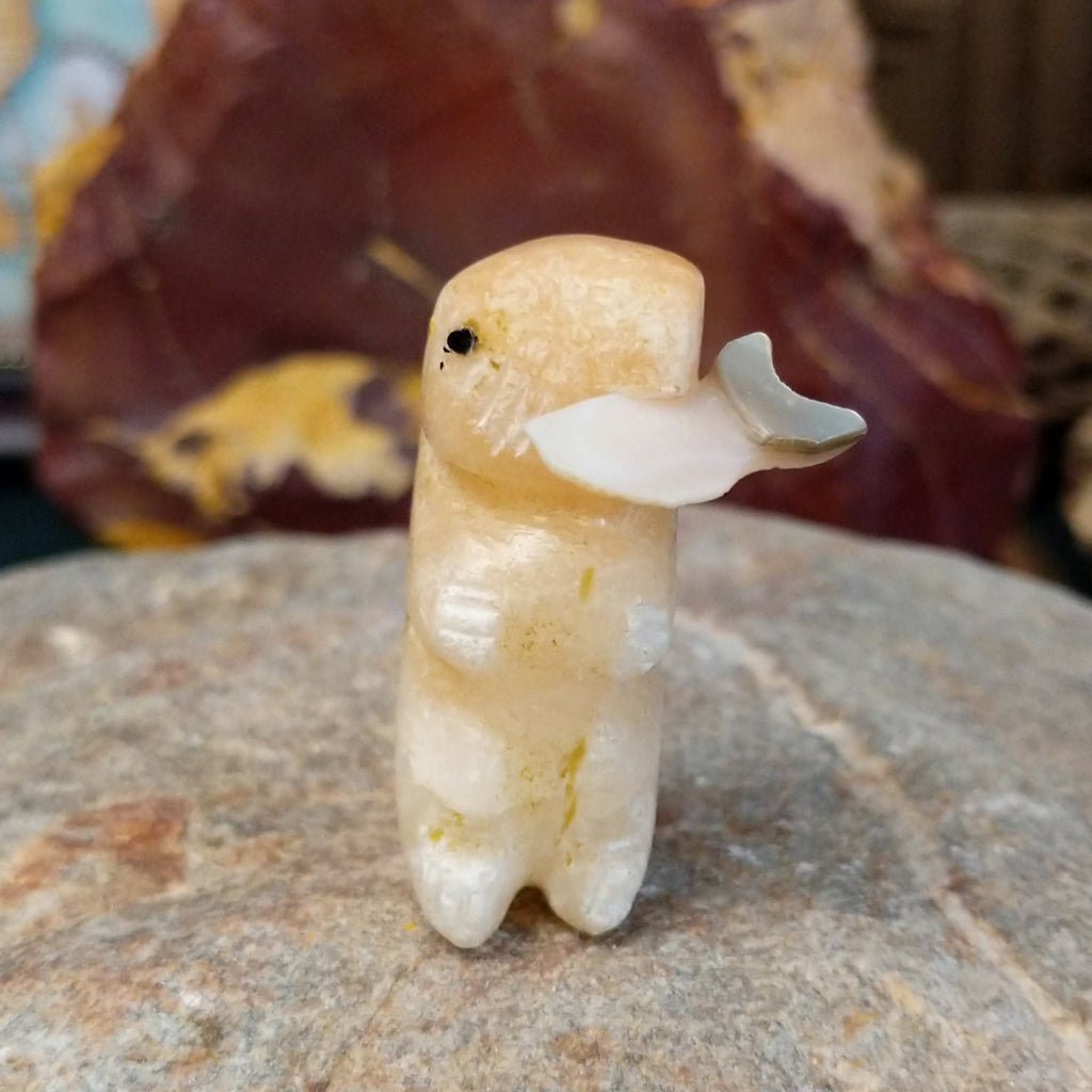 Light orange alabaster carved into an otter holding a fish in it's mouth and painted, black eyes.