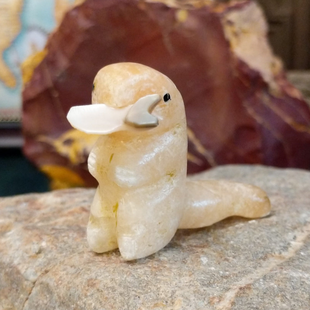Light orange alabaster carved into an otter holding a fish in it's mouth and painted, black eyes.