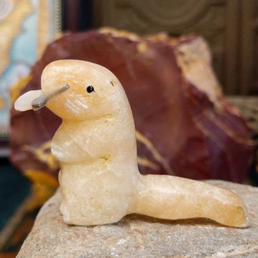 Light orange alabaster carved into an otter holding a fish in it's mouth and painted, black eyes.