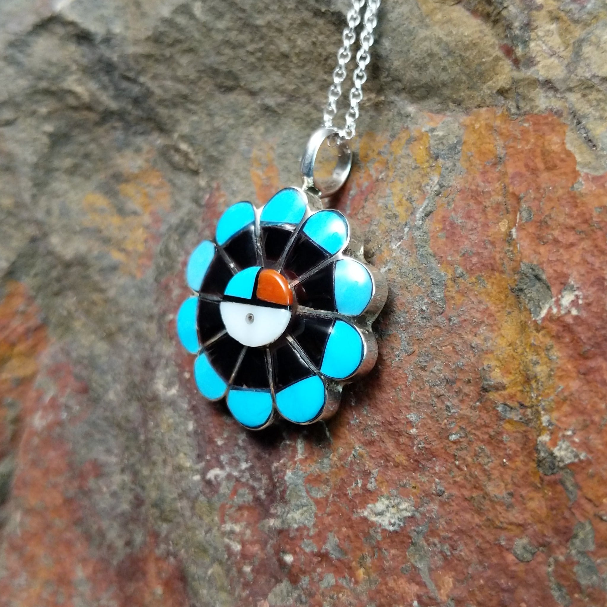 Handcrafted sterling silver Zuni Sunface pendant by R.V., featuring colorful multistone inlay in a traditional Sunface design; side view.