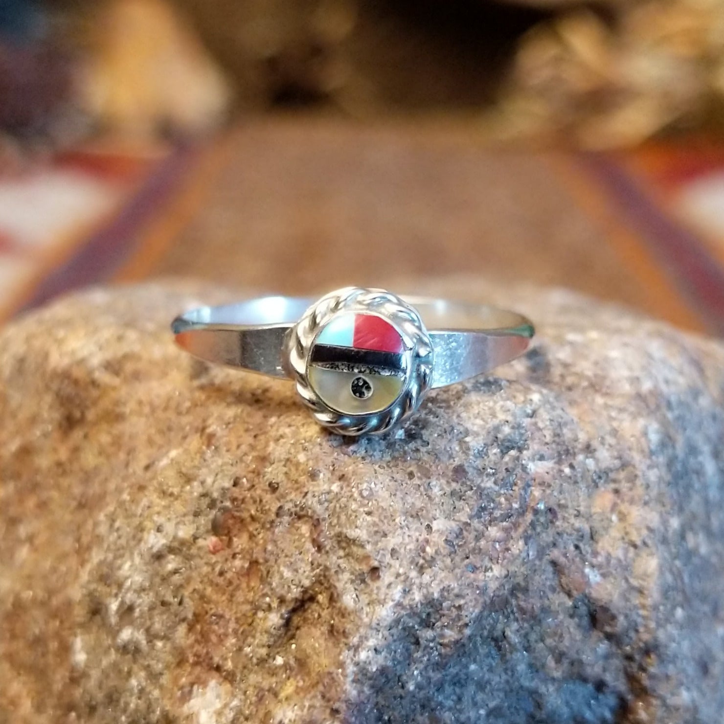 Sterling silver ring with sunface design crafted with turquoise, mother of pearl, black onyx, and coral that is framed by twisted rope detailing.