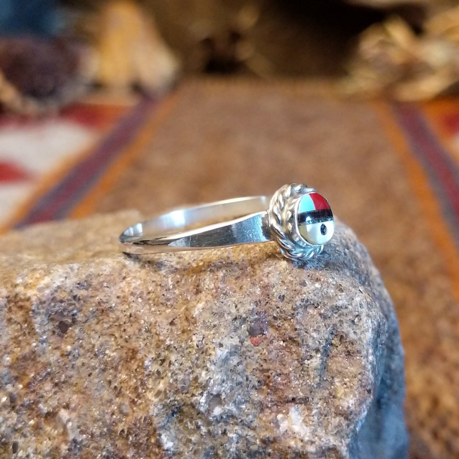 Sterling silver ring with sunface design crafted with turquoise, mother of pearl, black onyx, and coral that is framed by twisted rope detailing.