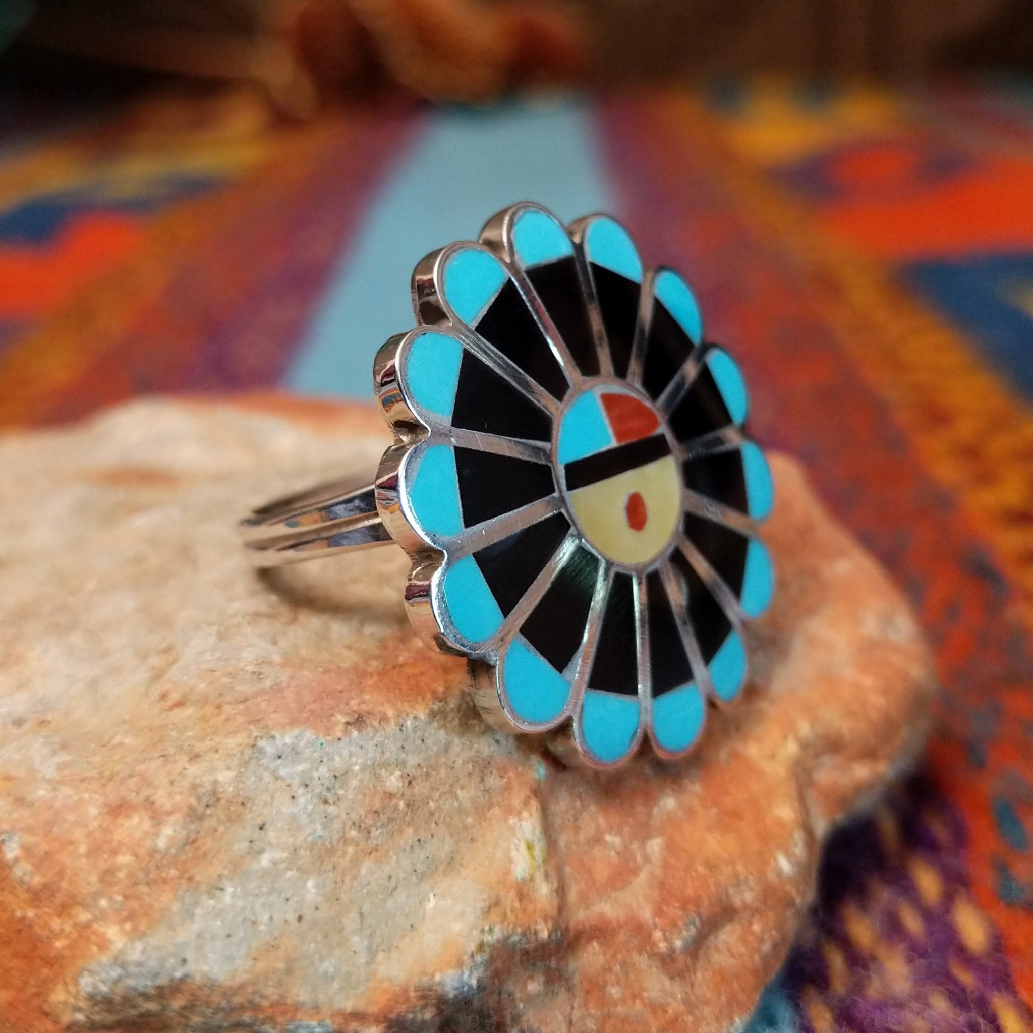 Zuni Sunface Ring by Annie Willie featuring an intricate multicolor inlay Sunface design with turquoise, black, red, and cream-colored accents set in Sterling Silver; side view.