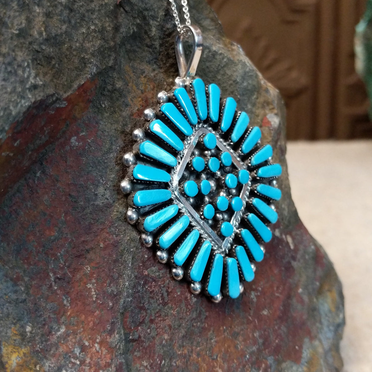 Zuni turquoise cluster pendant by Carlene Hattie featuring tapered and round turquoise stones arranged in an oval cluster with silver bead and twisted-wire detailing; side view.